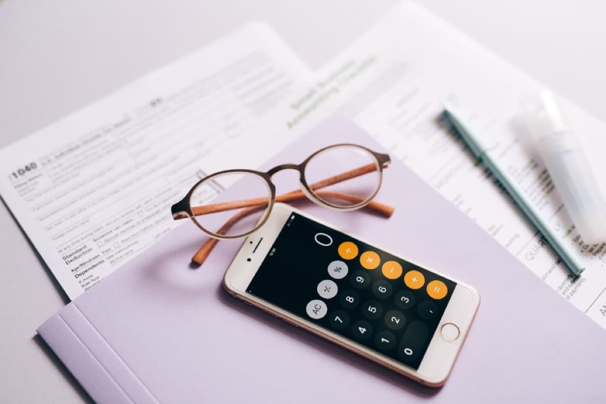 Tax forms, calculator app on a phone, and office supplies on a desk for organized bookkeeping